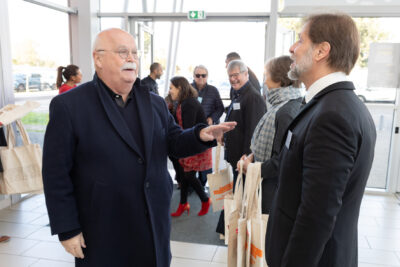 Photo de l'élu Bruno Lombardo qui échange avec M. Raynal à l'entrée du Phare, aux côtés d'autres élus qui distribuent des sacs aux personnes qui arrivent - Agrandir l'image 5 sur 14, fenêtre modale