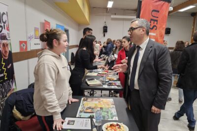 Le Maire échange avec une jeune femme debout derrière son stand d'information - Agrandir l'image 9 sur 13, fenêtre modale
