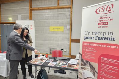 LE Maire échange avec une femme et montre du doigt de la documentation posée sur une table de stand. Sur la droite de la photo, on voit un kakémono sur lequel est écrit "chambre métiers artisanat Occitanie Haute-Garonne", "un tremplin pour l'avenir" - Agrandir l'image 12 sur 13, fenêtre modale