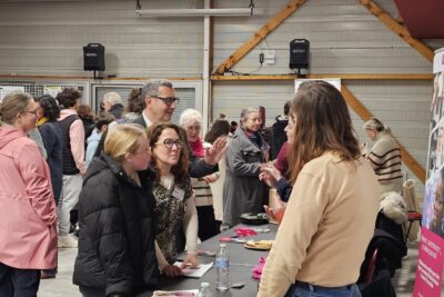 Des jeunes échangent avec des personnes rassemblées derrière un stand, on aperçoit de nombreux autres jeunes derrière ainsi que des adultes et le Maire Frédéric Parre - Agrandir l'image 2 sur 13, fenêtre modale