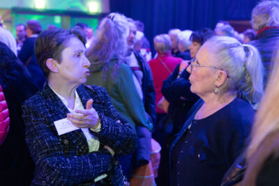 Deux femmes échangent entre elles. Derrière elle, on voit les nombreuses personnes présentes dans la salle - Agrandir l'image 19 sur 22, fenêtre modale