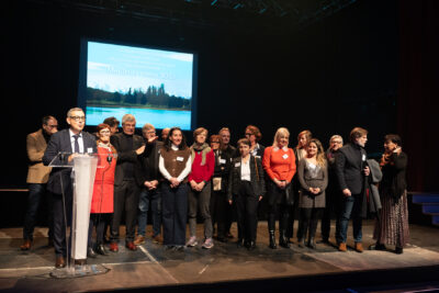 Photo de l'ensemble des élus de la majorité municipale qui se tiennent debout, rassemblés sur la scène. Devant eux sur la gauche, le Maire Frédéric Parre, fait un discours. - Agrandir l'image 11 sur 22, fenêtre modale