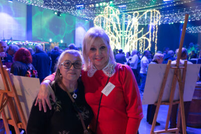 Deux femmes sourient à l'objectif, derrière elles, on voit le monde réuni dans la salle et la décoration lumineuse - Agrandir l'image 14 sur 22, fenêtre modale