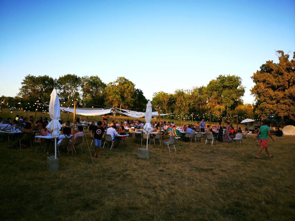 Photo de la guinguette de Tournefeuille, de nombreuses personnes réunies à table en plein air, dans un espace végétalisé - Agrandir l'image, fenêtre modale