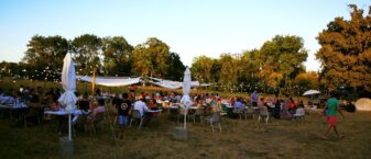 Photo de la guinguette de Tournefeuille, de nombreuses personnes réunies à table en plein air, dans un espace végétalisé