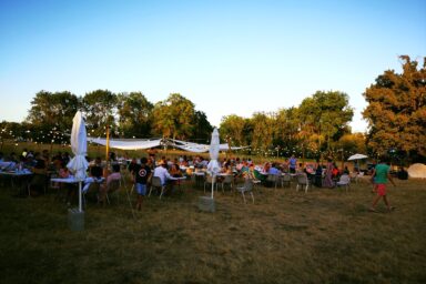 Photo de la guinguette de Tournefeuille, de nombreuses personnes réunies à table en plein air, dans un espace végétalisé