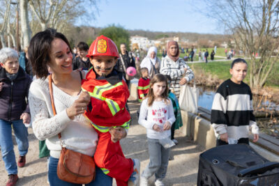 Photo de près d'une famille qui défile, un petit garçon est en costume de pompier, avec un maquillage de bouc et regarde l'objectif - Agrandir l'image 7 sur 18, fenêtre modale