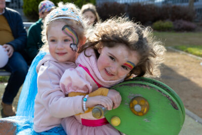 Deux jeunes filles sur un jeu à bascule pour enfants, maquillées avec un arc-en-ciel sur le front, et en costume rose - Agrandir l'image 14 sur 18, fenêtre modale
