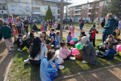 Photo du pique-nique dans le parc, de nombreuses familles avec jeunes enfants déguisés, installés par terre en train de goûter sous le soleil - Agrandir l'image 15 sur 18, fenêtre modale