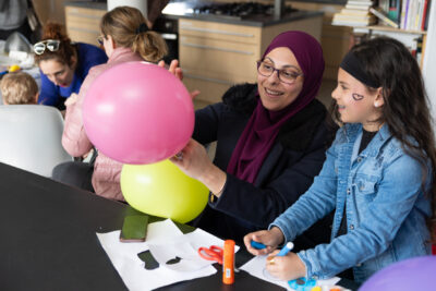 Photo d'une femme qui montre des ballons gonflés à une jeune fille qui a un coeur tatoué sur la joue - Agrandir l'image 3 sur 18, fenêtre modale