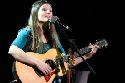 plan rapporché sur Lise Martin, guitare voix, en rpremière partie du concert de Claire Diterzi, cheveux long, visage expressif et teint diaphane, robe vert émeraude, chant au micro guitare en mains - Agrandir l'image 1 sur 8, fenêtre modale