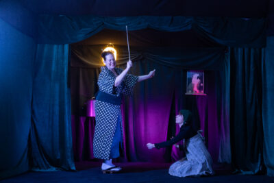 dans une scène de thé^tre encadrée de tentures de velours noir bleuté et nimbé d'une lumière rose, deux comédiennes vêtues d'habits traditionnels japonais se tiennent l'une debout la mère tenant une ombrelle, l'autre à droite de l'image, la petite Nozomi, agenouillée - Agrandir l'image 1 sur 7, fenêtre modale