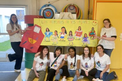 Photo de 7 femmes rassemblées autour d'un panneau où il est écrit "les héroînes de vos enfants" et des illustrations/photo montages des atsem en super héroïnes - Agrandir l'image 1 sur 8, fenêtre modale