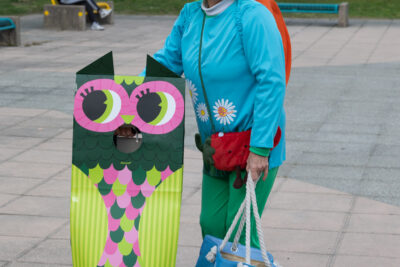 Photo d'une femme déguisée façon jardin, avec un haut bleu pour le ciel et bas vert pour l'herbe avec des fleurs, qui se tient debout à côté d'une chouette en carton et pose tout sourire pour l'objectif - Agrandir l'image 16 sur 28, fenêtre modale