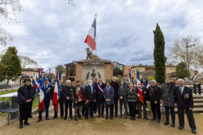Photo de groupe des élus rassemblés avec les porteurs de drapeaux devant le Monument aux morts, le ciel est gris - Agrandir l'image 16 sur 16, fenêtre modale