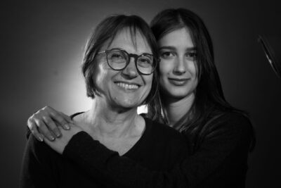 Photo d'une femme et d'une jeune femme derrière elle, la main sur son épaule, en noir et blanc, elles sourient à l'objectif - Agrandir l'image 19 sur 21, fenêtre modale