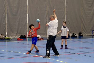 Photo d'un enfant qui s'apprête à lancer le ballon de handball, sur un terain de hand face à un homme - Agrandir l'image 14 sur 14, fenêtre modale
