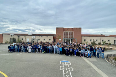 Photo de groupe dans la cour d'école, une centaine d'enfants et équipes pédagogiques rassemblées en bleu - Agrandir l'image 1 sur 14, fenêtre modale