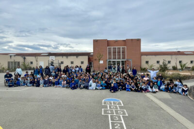 Photo de groupe dans la cour d'école, une centaine d'enfants et équipes pédagogiques rassemblées en bleu - Agrandir l'image 2 sur 14, fenêtre modale