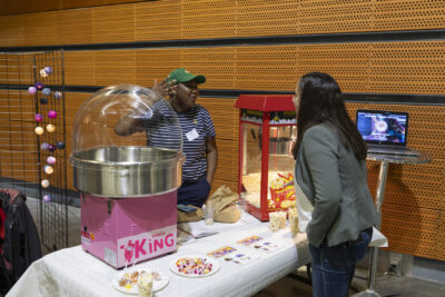 Deux femmes échangent à un stand de confiserie, il y a notamment une machine à pop corn et une machine à barbe à papa sur la table - Agrandir l'image 10 sur 20, fenêtre modale