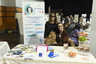 Deux femmes posent à un stand de coaching, derrière elles il y a un kakemono sur lequel il est écrit en titre "Votre singularité c'est vous" - Agrandir l'image 11 sur 20, fenêtre modale