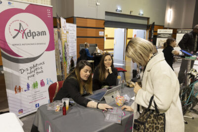 Une femme montre un dépliant à une autre femme, à un stand "Adpam, service autonomie à domicile" - Agrandir l'image 13 sur 20, fenêtre modale