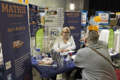 Un homme assis, de dos, échange avec une femme à un stand de chauffagiste - Agrandir l'image 17 sur 20, fenêtre modale