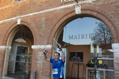 Photo d'un participant à la marche nordique qui sort de la Mairie et brandit ses bâtons en l'air - Agrandir l'image 6 sur 32, fenêtre modale