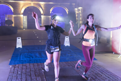 Photo de deux participantes au trail qui franchissent la ligne d'arrivée en se tenant la main, les bras en l'air et tout sourire - Agrandir l'image 11 sur 32, fenêtre modale