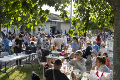 Photo paysage de nombreuses personnes rassemblées sur une place ensoleillée et dans la verdure, pour partager un repas