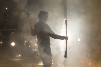 Une homme jongle avec des bâtons en feu au milieu de feu d'artifices - Agrandir l'image 53 sur 53, fenêtre modale