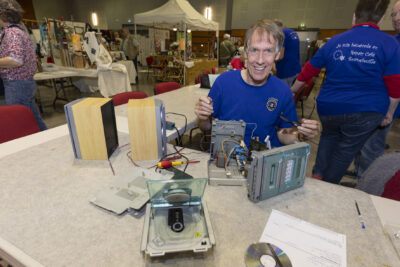 Un bénévole du Repair café travaille tout sourire sur une chaîne hifi en panne - Agrandir l'image 12 sur 17, fenêtre modale