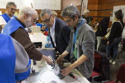Le Maire Frédéric Parre observe les bénévoles du repair café étudier un petit appareil en panne - Agrandir l'image 5 sur 17, fenêtre modale