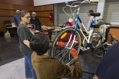Stand de réparation de vélo, une personne est en train de manipuler la roue de devant, une femme à côté - Agrandir l'image 14 sur 17, fenêtre modale
