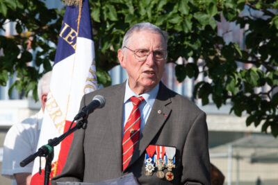 Photo d'un homme portant de nombreuses médailles qui fait un discours, on voit le drapeau français derrière lui - Agrandir l'image 4 sur 5, fenêtre modale