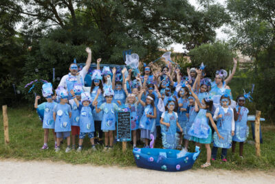 Photo d'un groupe d'enfants réunis avec des animateurs, habillés tous en bleu, devant eux une sorte de petite barque bleue faite à la main - Agrandir l'image 23 sur 24, fenêtre modale