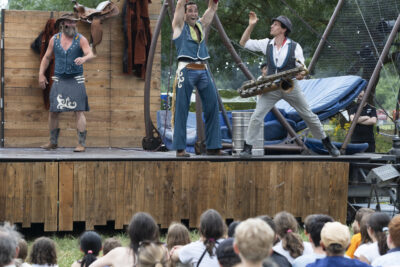 Photo portrait d'un spectacle sur scène, trois hommes en costume et le public au premier plan avec beaucoup d'enfants - Agrandir l'image 6 sur 24, fenêtre modale