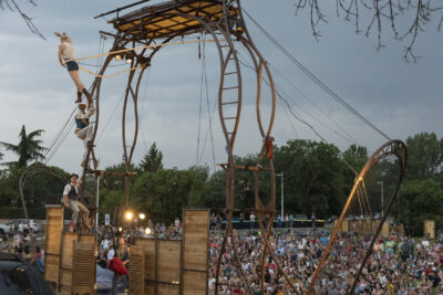 Photo paysage d'acrobates sur scène, vue de derrière, avec le public nombreux installé dans l'herbe - Agrandir l'image 4 sur 24, fenêtre modale