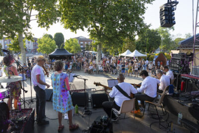 Photo paysage prise depuis le scène sur le parvis de la Mairie, un groupe se produit et on voit le public un peu éloigné à l'ombre qui profite du concert - Agrandir l'image 12 sur 16, fenêtre modale