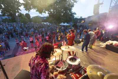 Photo paysage prise depuis l'angle de la scène au niveau du batteur, avec vue sur le public nombreux tandis que l'après-midi touche à sa fin - Agrandir l'image 1 sur 16, fenêtre modale