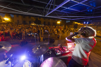 Photo paysage depuis la scène jeunesse derrière la Mairie, un ado blond de dos est DJ, une foule de jeunes est présente devant la scène - Agrandir l'image 10 sur 16, fenêtre modale