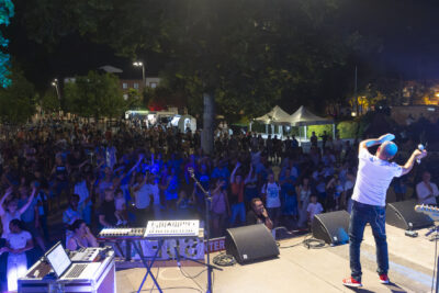 Photo paysage prise depuis la scène Place de la Mairie, un homme sur scène met les bras en l'air sur le côté et la foule rassemblée devant l'imite - Agrandir l'image 4 sur 16, fenêtre modale
