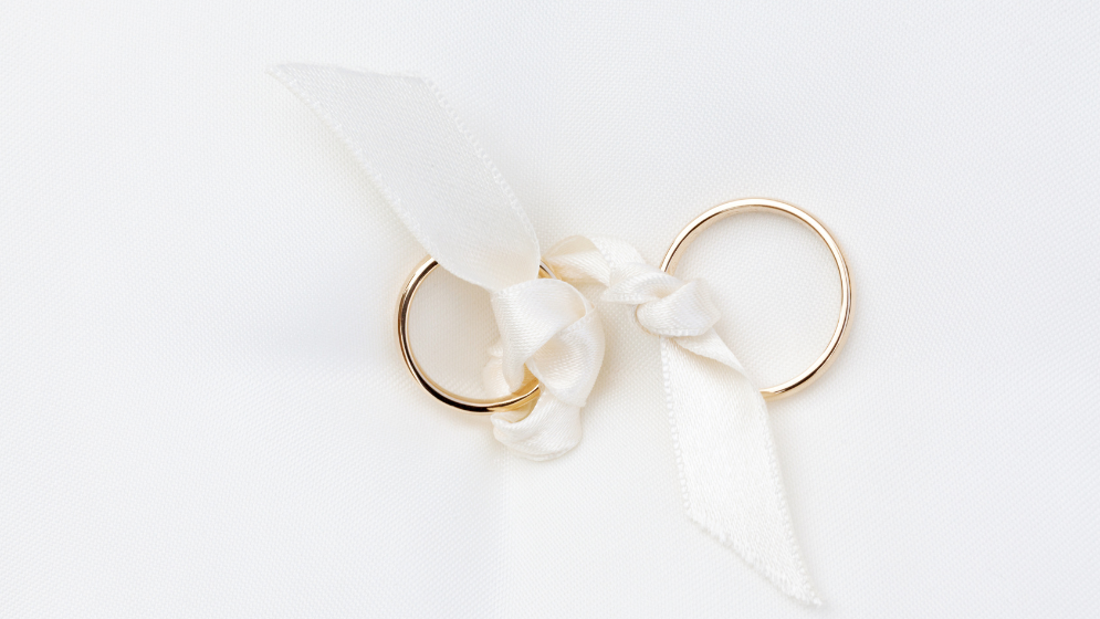 Photo de deux alliances nouées par un ruban blanc, posées sur un fond blanc