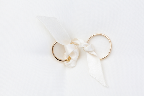 Photo de deux alliances nouées par un ruban blanc, posées sur un fond blanc