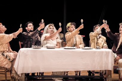 Des personnages de théâtre, endimanchés, lèvent leur cuillère autour d'une tablée nappée. - Agrandir l'image, fenêtre modale