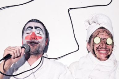 Deux hommes grimés et habillés en blanc, l'un avec un maquillage de clown, l'autre portant une toque de cuisinier, des concombres à la place des yeux.