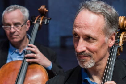 Plan rapproché sur deux solistes de l'orchestre en train de jouer de leur instrument à cordes en souriant, habillés à l'unisson, chemise bleu pétrole et verste noire élégante. - Agrandir l'image, fenêtre modale