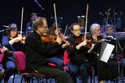 lan rapproché sur les musiciens de l'Orchestre Symphonique de l'Ecole de musique de Tournefeuille, violons visibles au premier plan, vêtus de noir, assis sur des chaises à dossier rouge. - Agrandir l'image, fenêtre modale