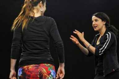 photo montrant à droite de profil la chorégraphe et danseuse Stéphanie Fuster cheveux attachés bruns et le sourire, en survêtement de sport s'aidant des mains pour expliquer un élément de son propos à une jeune femme de dos tee shirt noir et jupe fleurie