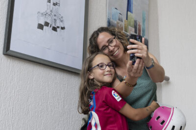 Une mère souriante cheveux bouclés châtain et lunettes en écaille et sa fillette qui lui ressemble en robe fuschia se prennent en photo à l'aide d'un smartphone devant un grand tableau exposé dans l'escalier de l'Ecole d'enseignements artistiques de Tournefeuille - Agrandir l'image 3 sur 7, fenêtre modale